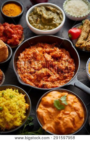 Various Indian dishes on a table. Spicy chicken Tikka Masala in iron pan. Served with rice, naan and spices. Set of different kind Indian food.