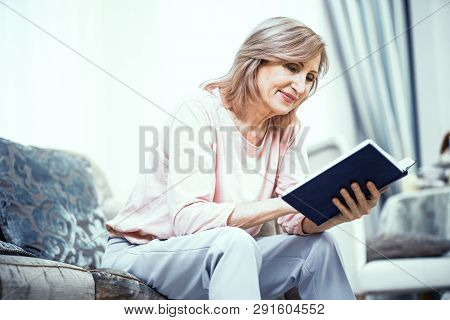 Nice Middle Aged Woman Sitting On Sofa And Attentively Reading Bible. Religion Concept.