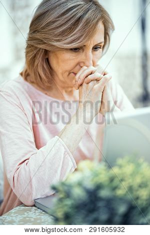 Close Up Attentive Look Of An Elderly Woman. Folding Her Palms In Front Of Her Face She Looks At The