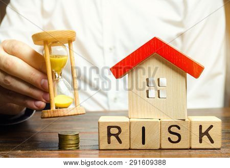 Businessman Holds Clock, Wooden House And The Inscription Risk On Wooden Block. The Concept Of Non-p