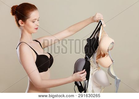 Bosom Concept. Slim Attractive Red Hair Woman Wearing Black Underwear Holding Many Bras In Hand, Cho