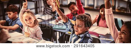 Schoolkids raising their hands in classroom at school