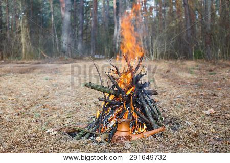 At The Stake In The Spring Forest, A Clay Turkish Coffee Pot Is Heated Against The Grass.