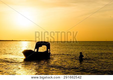 Silhouette Of Man Carrying The Anchor Of Boat Out To Sea