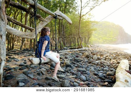 Young Female Tourist Relaxing On A Handmade Swing On Rocky Beach Of Pololu Valley On Big Island Of H