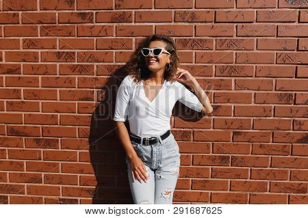 Attarctive Elegant Young Woman Hipster In A White Sunglasses In A Summer Denim Pants And White T-shi