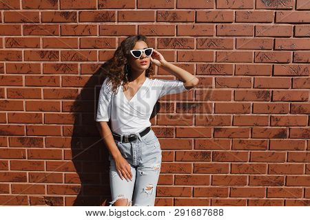 Attarctive Elegant Young Woman Hipster In A White Sunglasses In A Summer Denim Pants And White T-shi