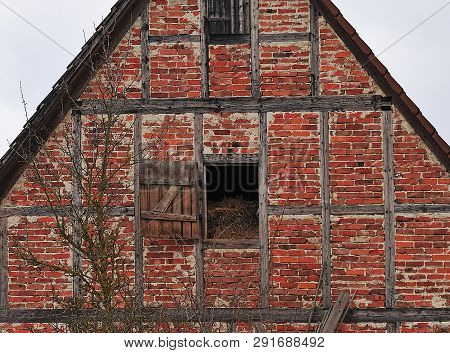 Old Farmhouse With Half-timbered Facade And Hay Stored In The Attic To Be Seen Through Open Window