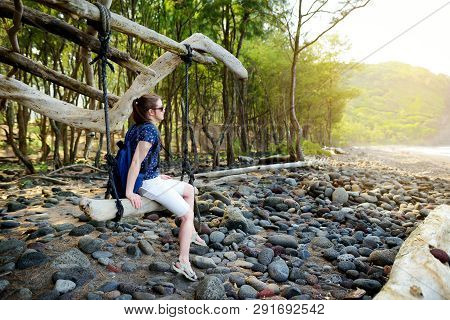 Young Female Tourist Relaxing On A Handmade Swing On Rocky Beach Of Pololu Valley On Big Island Of H