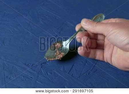Closeup Of A Male Hand Holding A Dirty Silverspoon Above The Blue Painted Table