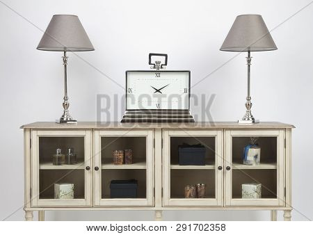 Glass Fronted Sideboard And Ornaments With Lamps And A Large Clock On A White Background