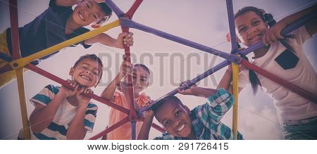 Portrait of happy schoolkids looking through dome climber at school playground