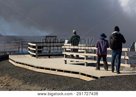 REYKJANES PENINSULA, ICELAND - APRIL 29, 2018: Steaming vents at Gunnuhver geothermal area in Iceland, viewing platform at a touristic lookout spot with tourists sightseeing