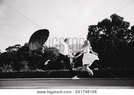 Young Couple Jump Up With Black Upbrella. Lovely Cuople Have Fun