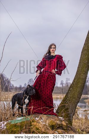 Art Photography Concepts. Beautiful Fairy Princess In Red Dress With Crown And Her Dog On Leash In F