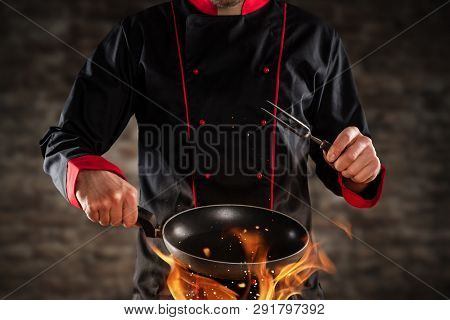 Closeup of chef holding empty frying pan above grill. Concept of food preparation, ready for product placement.