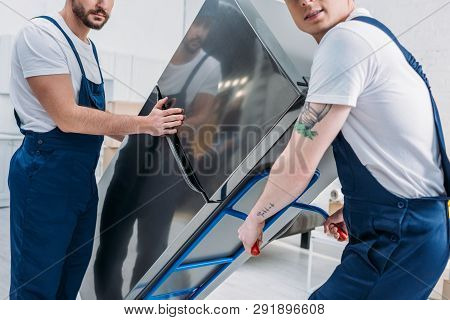 Cropped View Of Two Movers Using Hand Truck While Transporting Refrigerator In Apartment