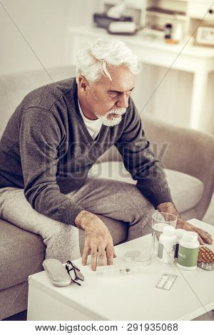 Elderly Man Sitting At Table Full Of Pills Boxes