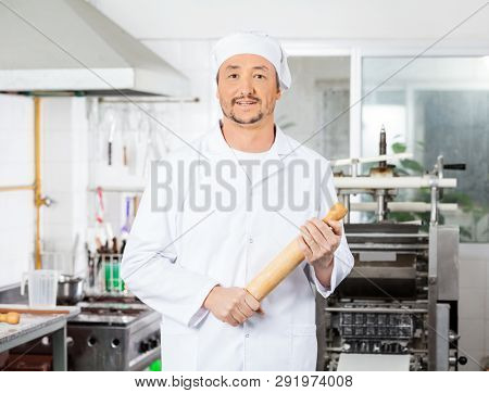 Confident Male Chef Holding Rolling Pin In Kitchen