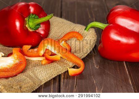Group Of Two Whole Four Slices Of Bulgarian Red Bell Pepper On Jute Cloth On Brown Wood