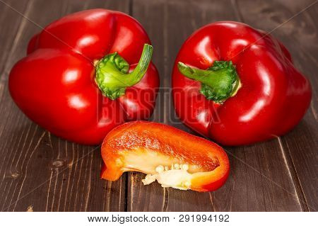 Group Of Two Whole One Slice Of Bulgarian Red Bell Pepper On Brown Wood