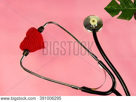 Knitted Red Heart With A Phonendoscope On A Pink Background. Heart Disease Patient Support Concept