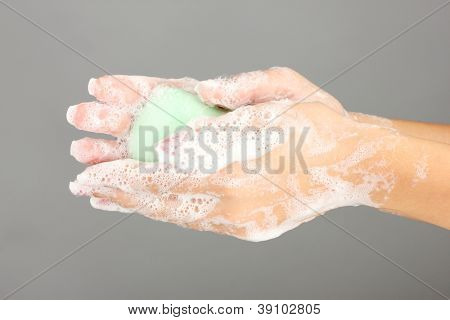 มือของผู้หญิงใน soapsuds บนพื้นหลังสีเทาอย่างใกล้ชิด
