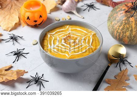 Halloween Pumpkin Soup With Creamy Spider Web In Gray Bowl And Spiders On The Table. Closeup