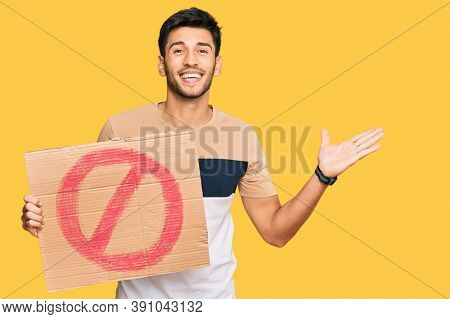 Young handsome man holding prohibited warning banner celebrating victory with happy smile and winner expression with raised hands 
