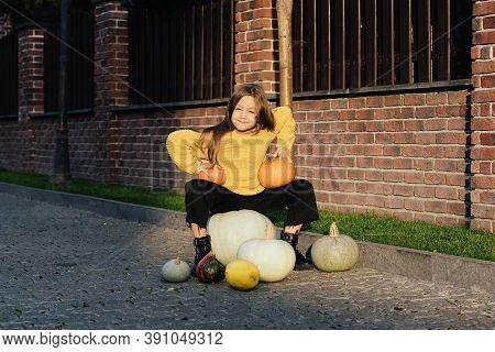 Funny Child Girl In Orange Pullover For Halloween With Pumpkin And On A Dark Brick Background.