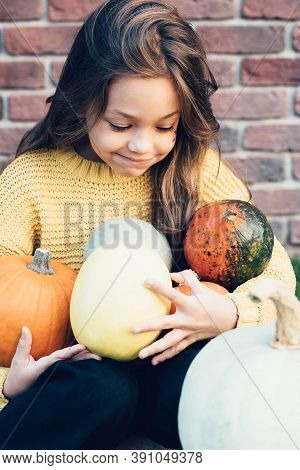 Funny Child Girl In Orange Pullover For Halloween With Pumpkin And On A Dark Brick Background.