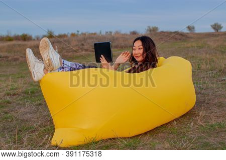 Pretty Young Asian Woman Sitting On A Yellow Lamzak Having A Video Chatting With Tablet On A Cliff N