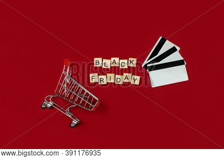 Black Friday Phrase Made Of Wooden Blocks, Shopping Cart And Credit Cards Flat Lay On Red Background