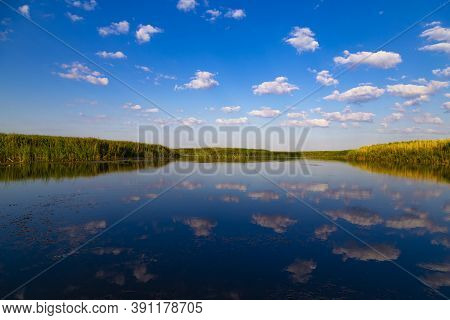 Scenic View Over The Lake. White Clouds On Blue Sky Are Mirrored  Reflected In The Water Surface. Na