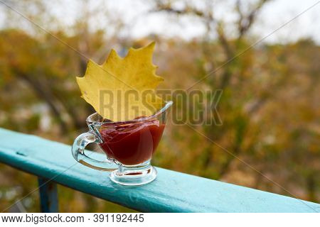 Yellow Autumn Leaf In A Glass Gravy Boat With Red Ketchup Stands On A Blue Railing In Front Of An Au
