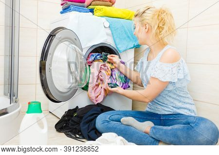 Woman In Bathroom Sorting Different Colored Clothes Laundry For Washing In Machine, Using Detergent 
