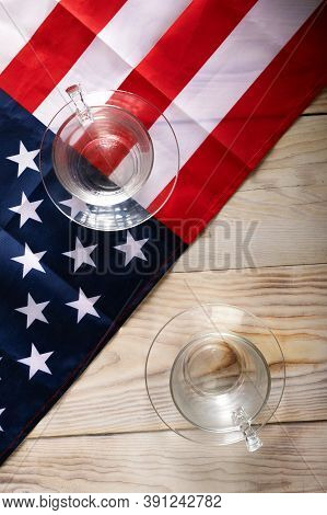 Two Glasses Opposite Each Other On Background Of American Flag. The Concept Of Battling In Us Presid