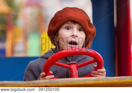 Photo Of Amazed Girl In Red Cap Keeping Red Steering Wheel On A Playground. Close Up Portrait Of Cut