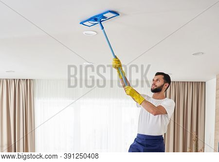 Man Cleaning Ceiling And Lamps In Living Room. House Cleaning Service Concept.
