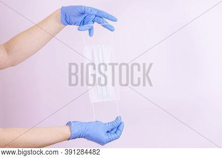 Blue-gloved Hand Holds A Medical Mask. Covit-19 Coronavirus Pandemic