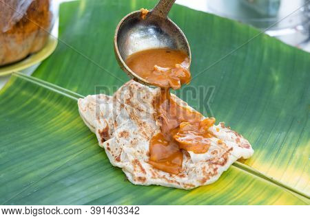 Curry Being Poured Onto Roti Canai Or Paratha Served On Banana Leaf