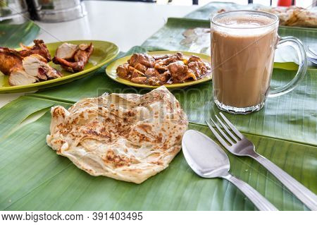 Roti Canai Or Paratha Served On Banana Leaf, With Mutton Curry And Fried Chicken, And Popular Teh Ta