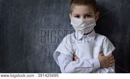 A Serious, Focused Boy In A Medical Mask And A White Coat, Stands Against The Background Of A Black 