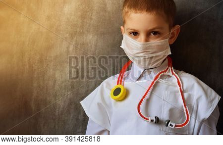 A Serious, Focused Boy In A Medical Mask And A White Coat, Stands Against The Background Of A Black 