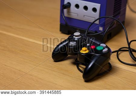 A Black Gamecube Controller Plugged Into The Indigo Gamecube On A Wood Floor