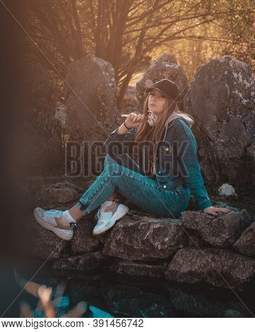 Portrait Of An Attractive Brunette Sitting In A Stone Well At The Rajcica Wells Landmark. Wearing Je