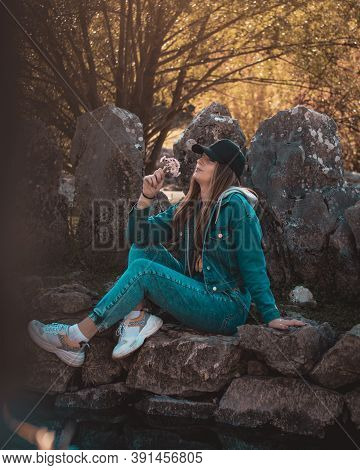 Portrait Of An Attractive Brunette Sitting In A Stone Well At The Rajcica Wells Landmark. Wearing Je