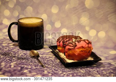 Two Fresh Donuts In Pink Glaze With Chocolate And Powdered Sugar On A Plate And A Cup Of Cappuccino