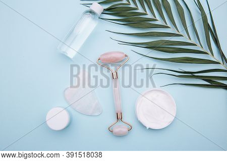 Pink Roller Face Massager And Gouache Scraper On Blue Background. Beauty Care Concept