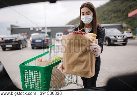Over Trunk View Of Young Woman In Medical Mask In Masks Loading Bags In Trunk After Supermarket Shop